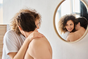 Side view of curly young woman and brunette man in bathroom hugging in love and smiling