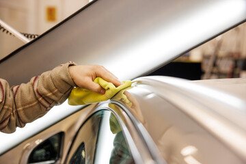 Person cleaning car with yellow cloth on hood and rims - obrazy, fototapety, plakaty