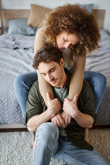 Lovely woman hugging her relaxed boyfriend from behind sitting on bed smiling together