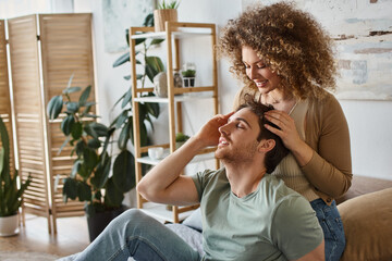 curly young woman gently massaging boyfriends head smiling together in bedroom