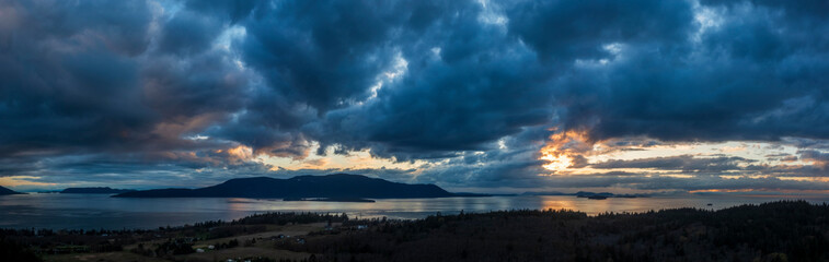 Panoramic aerial sunset over Orcas Island with dramatic clouds. Seen from Lummi Island and looking across Rosario Strait in the San Juan Islands area of western Washington state.  - 770854969