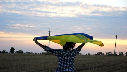 Ukrainian woman walking on barley meadow with a blue-yellow banner on shoulders at sunset. Lady...