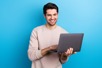 Fototapeta na wymiar Portrait of satisfied pleasant guy with brunet hair wear light pullover look at laptop typing message isolated on blue color background