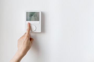 Cropped shot of woman hand setting room temperature on thermostat at home
