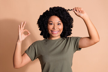 Photo of attractive woman with afro hairstyle wear khaki t-shirt touch curl show okey like new hairdo isolated on beige color background