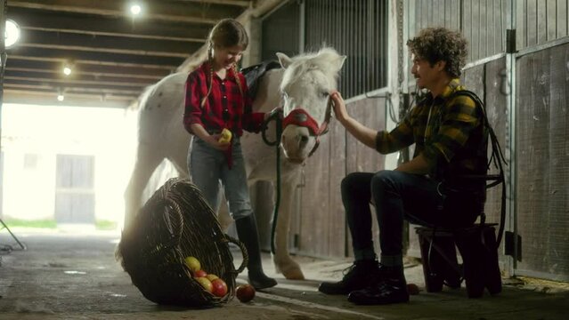 Horse owners a farmer and his young daughter feed a horse in a barn on a family ranch