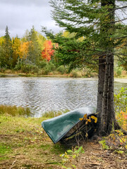 Classic green canoe resting against a tree near a country lake in autumn