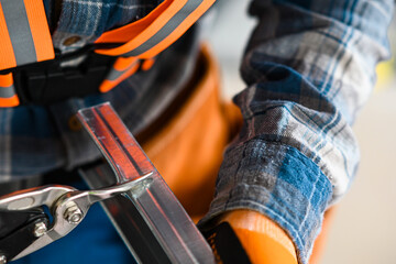 a construction worker in overalls, gloves and a tool belt cuts an iron profile for plasterboard...