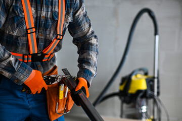 a construction worker in overalls, gloves and a tool belt cuts an iron profile for plasterboard...