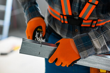 a construction worker in overalls, gloves and a tool belt cuts an iron profile for plasterboard...