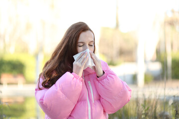 Woman walking down the street in winter blowing her nose