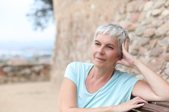 Mature woman is relaxing sitting on a bench looking around