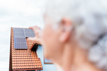 Close up shot of solar panel on the roof with blurred retried woman on foreground.