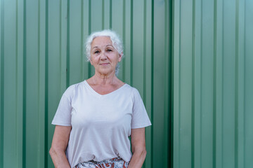Grey haired 60s woman poses in front of a gray metal fence with vertical bands.