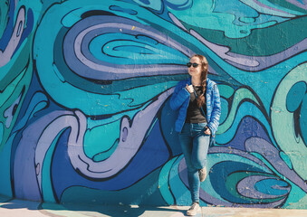 Relaxed young smiling female in jeans and blue jacket near graffiti wall on Belgrade city street, Serbia