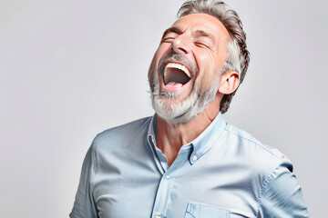 An elderly man in a blue shirt with a beard laughs loudly , gray background