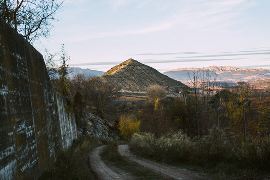 Dry hill scenery in the last rays of light a car road and a wall on the left