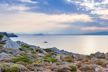Fototapeta na wymiar deserted seashore of northern Crete in the light of sunset, fishing boat on the sea, Greece