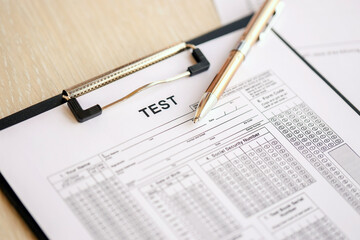 Blank educational test for students lies on table in classroom with pen close up