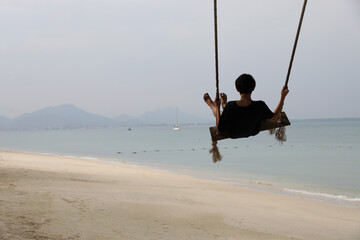 Young asian boy on a swing by the sea looking at sea, Vacation and travel concept.