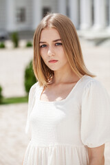 Portrait of a young beautiful blonde girl in a white summer dress with open shoulders