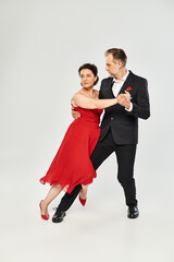 Ballroom dance middle aged couple in red dress and suit dancing tango isolated on grey background
