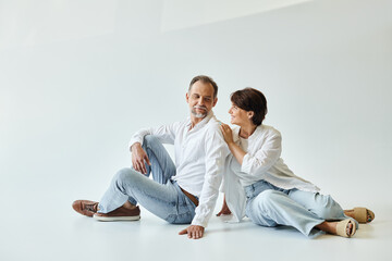 Full length shot of mature beautiful couple sitting on grey background and looking at each other