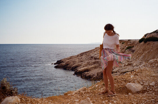 Young woman standing on a rock and the wind blows her skirt away