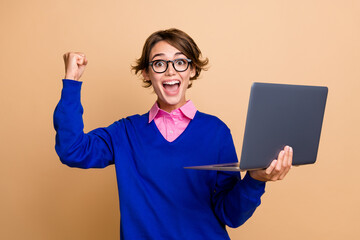 Portrait of successful overjoyed lady use laptop raise fist shout yeah hooray isolated on beige...