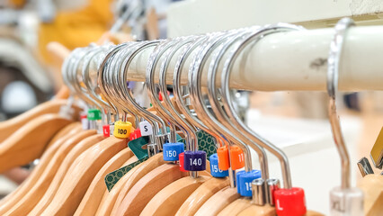 Close-up view and selective focus of empty wooden hangers with colorful plastic size tags indexes of the S, M, L, XL, 100, 140, 150, 160 displayed in store for sale
