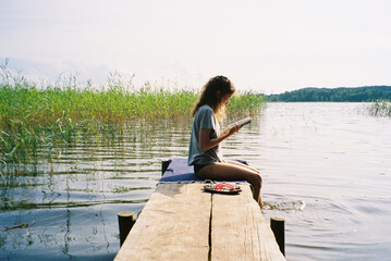 Young woman sitting on wooden pier and reading book