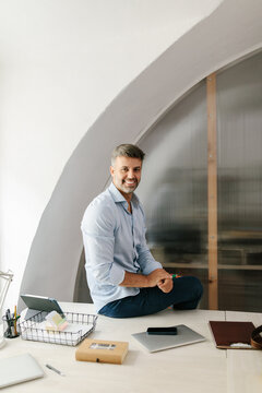 Smiling businessman sitting at office desk looking at camera