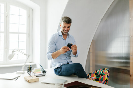Portrait of a man smiling and using phone in office 