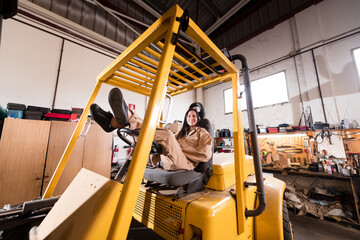Carefree female worker sitting on forklift at workshop