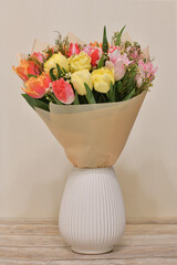 A bouquet of flowers in ceramic vase stands on a table in the room