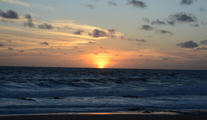 Fototapeta premium sunset at sea, with orange sky and the sun setting on the beach horizon