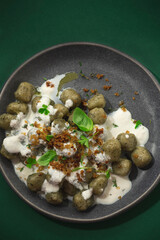 Integral gnocchi with wild herbs and ricotta sauce on a green dark background. Proper nutrition, traditional recipes of Northern Italy in a new interpretation