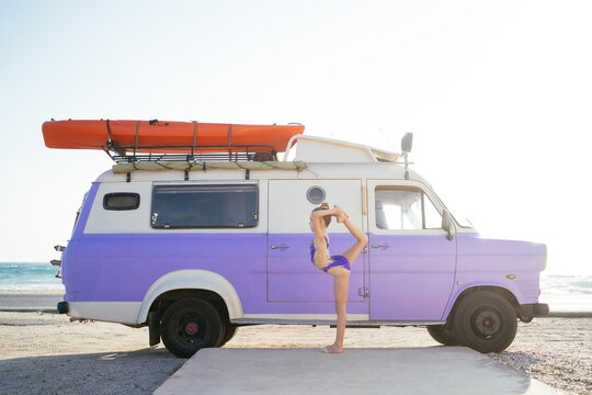 Gymnast with leg behind back near caravan on sunny beach