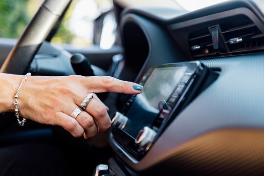 Woman's hand pressing the touch screen in her car. Selects an application on the screen of car computer.