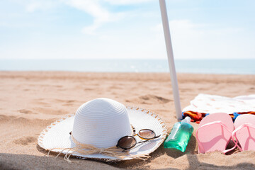 Close up of beach accessories on sand hat, sunglasses, sun cream, flip flops, towel and umbrella...