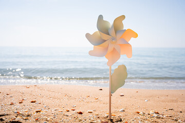 Fototapeta na wymiar Toy pinwheel stuck in the sand of a beach with the sea in the background on a beautiful summer morning