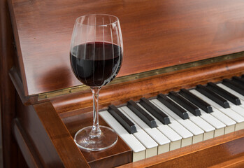 a glass of red burgundy wine in an elegant etched wineglass resting on a piano keyboard