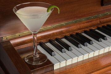 a gin martini cocktail with a zest of lime in a martini glass on a piano keyboard
