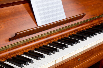 a close up angle view of a rosewood piano keyboard with blank sheet music staff paper