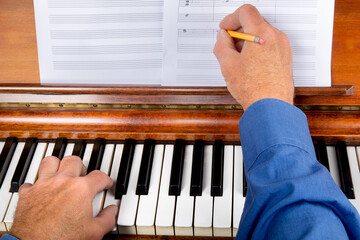 close up of a composer marking notes on staff paper as he plays the piano