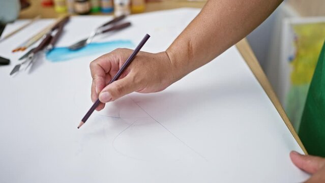 Passionate young latin artist immersed in drawing on his notebook, stationed at the heart of a vibrant art studio