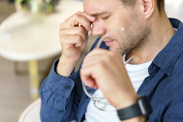 A close-up depicts a man in deep thought or concern, holding his glasses in a moment of pause.