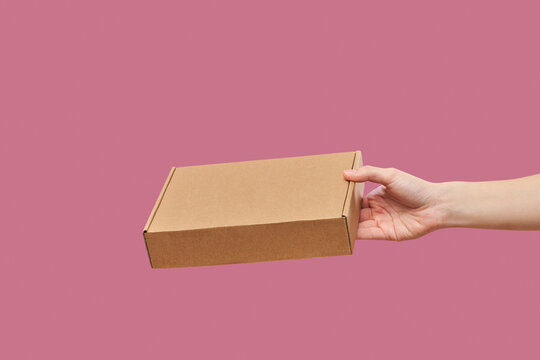 Female hand delivering cardboard parcel box over purple background