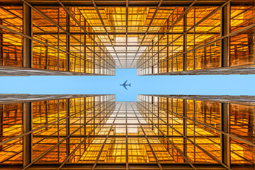 Looking up a golden symmetrical skyscraper to an flying aircraft in the very blue sky