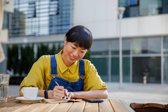 Smiling freelancer writing important notes in book at cafe 